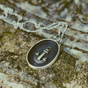 May include: A silver chain necklace with a round pendant featuring a black anchor design.