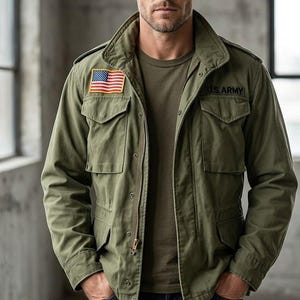 Könnte beinhalten: Olivgrüne Jacke im Militärstil mit einem amerikanischen Flaggenaufnäher und dem Text "U.S. ARMY". Die Jacke hat mehrere Taschen und einen Reißverschluss. Die Person trägt ein grünes T-Shirt und dunkelblaue Jeans.