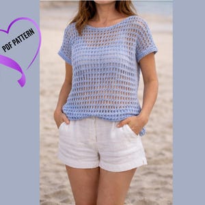 Może przedstawiać: Jasnoniebieski top z szydełka z krótkimi rękawami i okrągłym dekoltem. Top jest połączony z białymi szortami. Obraz zawiera tekst "PDF PATTERN" w fioletowej grafice w kształcie serca.
