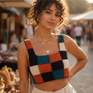 May include: A sleeveless crop top featuring a multi-coloured checkered pattern in black, burnt orange, teal, and cream. The garment is constructed with a crochet knit texture, a square neckline, and wide shoulder straps, ending at the midriff.