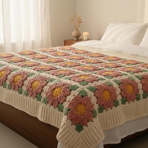 Puede incluir: Una manta de ganchillo hecha a mano con un patrón floral. La manta presenta grandes motivos florales cuadrados en tonos de rosa, amarillo y verde, sobre un fondo crema. La manta está colocada sobre una cama, mostrando su intrincado diseño.