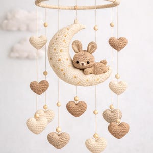May include: A handmade crochet baby mobile featuring a crescent moon with gold star accents and a small bunny. The mobile includes hanging crochet hearts in cream and brown tones, suspended from a circular frame.