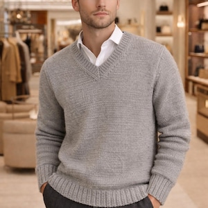 May include: A light gray V-neck sweater over a white collared shirt. The sweater has ribbed cuffs and hem. The person is wearing dark gray pants and has their hands in their pockets.