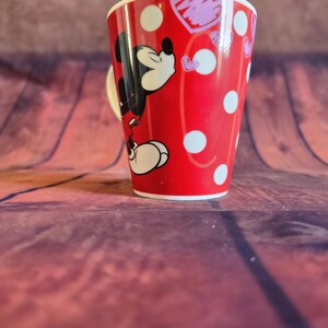 Puede incluir: Taza de cer&aacute;mica roja con Mickey Mouse, lunares blancos y un coraz&oacute;n. La taza tiene un asa y borde blancos. Ideal para t&eacute; o caf&eacute;, mide unos 10 cm de altura.