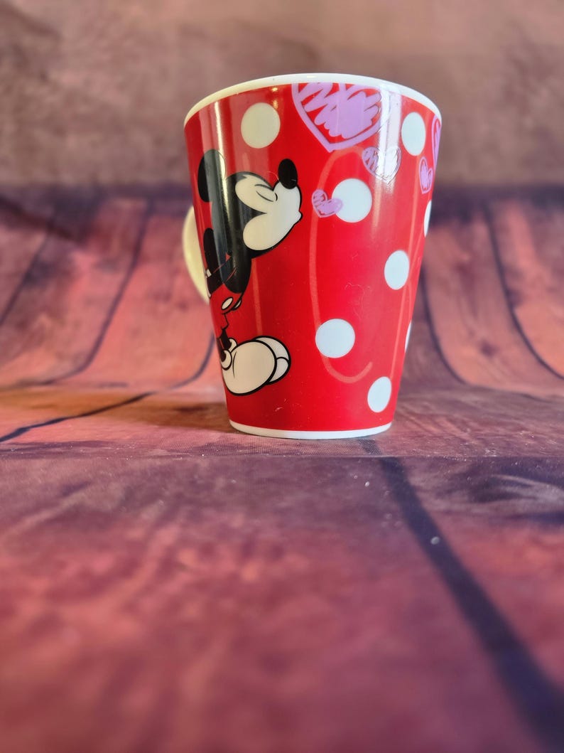 Puede incluir: Taza de cer&aacute;mica roja con Mickey Mouse, lunares blancos y un coraz&oacute;n. La taza tiene un asa y borde blancos. Ideal para t&eacute; o caf&eacute;, mide unos 10 cm de altura.