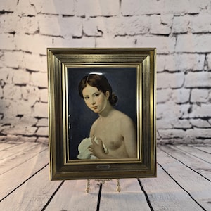 Peut inclure: Tableau encadré d'une femme tenant un tissu blanc. Le tableau est encadré dans un cadre doré et exposé sur un présentoir décoratif. L'arrière-plan est sombre.