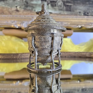 Peut inclure: Un récipient décoratif argenté métallique détaillé avec un couvercle. Le récipient présente un motif texturé semblable à du tissage et est soutenu par une base circulaire et des supports verticaux. Le couvercle est surmonté d'un petit élément décoratif.