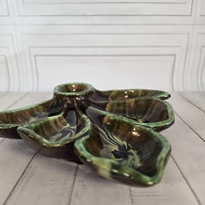 Puede incluir: Un plato de cerámica vintage con un diseño en forma de hoja. El plato presenta un compartimento central circular y cinco secciones circundantes en forma de hoja. La combinación de colores incluye tonos de marrón, verde y negro, con un acabado brillante. Está diseñado para servir aperitivos.