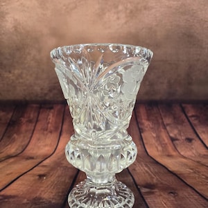 Peut inclure: Un vase en verre taillé transparent avec un dessus évasé et une base en piédestal. Le vase présente des motifs floraux et géométriques complexes, avec un design détaillé autour du bord et de la base. Le vase est conçu pour contenir des fleurs.