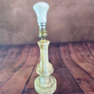 Peut inclure: Un pied de lampe de table en pierre d'onyx polie aux tons beige et crème, présentant une silhouette lisse et profilée. La lampe est dotée d'une douille en métal doré, équipée d'une ampoule blanche en forme de poire et d'un cordon blanc.