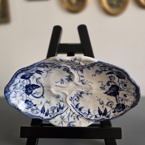 Peut inclure: Un plat en porcelaine bleu et blanc avec un motif floral. Le plat est sur un petit chevalet noir.