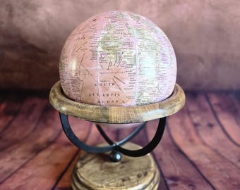Globo terráqueo decorativo rosa sobre soporte de madera y metal.