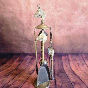May include: Vintage brass fireplace tool set featuring horse head detailing. The set comprises a shovel, poker, and brush, suspended from a central stand. The tools are arranged on a circular base, with a horse head finial at the top.
