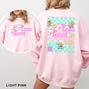 A woman wearing a pink sweatshirt with a design featuring the characters from the animated film "Pizza Planet".