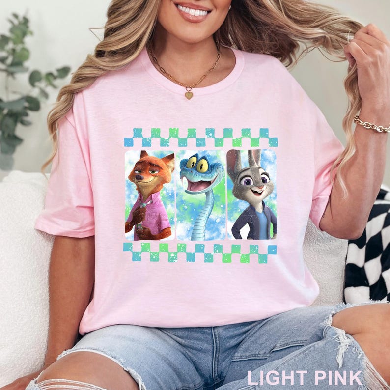 May include: Light pink t-shirt featuring a graphic of three cartoon characters: a fox, a snake, and a rabbit. The graphic is framed by a blue and green checkered pattern. The text "LIGHT PINK" is printed at the bottom of the shirt.