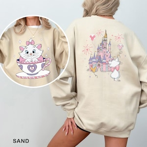 A person wearing a beige sweatshirt with a cartoon image of a cat sitting in a teacup and a castle in the background.
