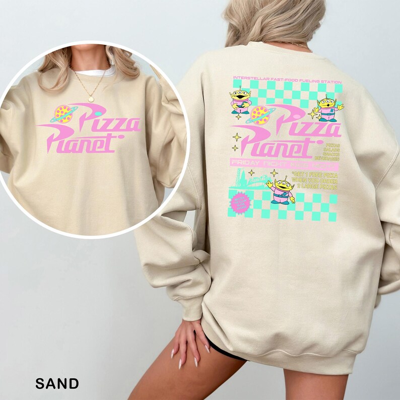 A person wearing a beige sweatshirt with a colorful design featuring the characters from the animated series "Pizza Planet".