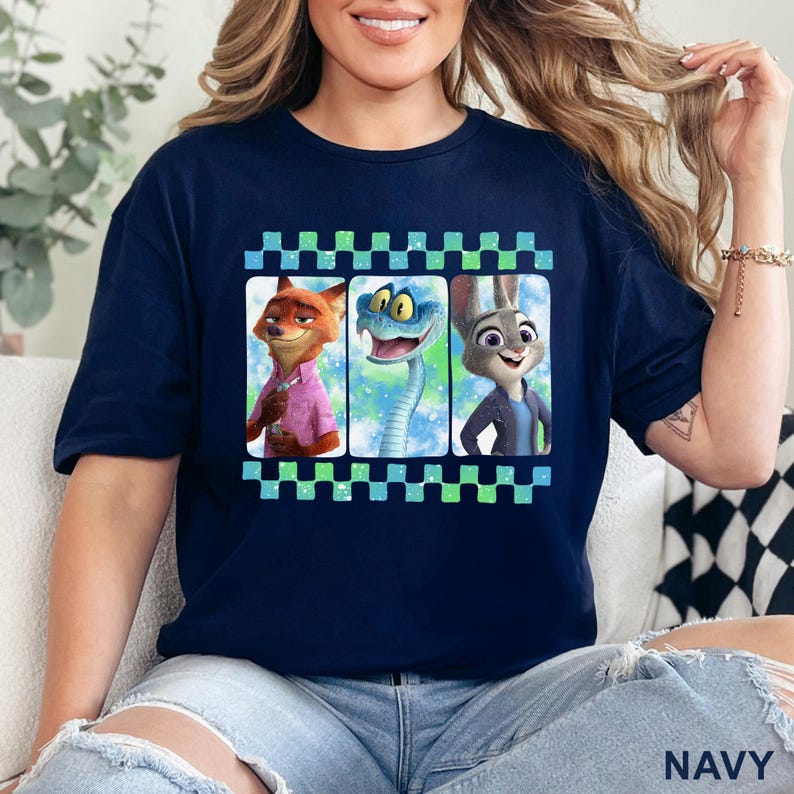 May include: Navy blue t-shirt featuring three characters from Zootopia: Nick Wilde, a snake, and Judy Hopps. The characters are in individual frames with a checkered border. The word "NAVY" is printed at the bottom of the shirt.