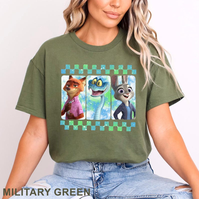 May include: Military green t-shirt featuring a graphic of three animated characters: a fox, a snake, and a rabbit. The characters are set against a blue and green checkered background. The shirt's color is military green.