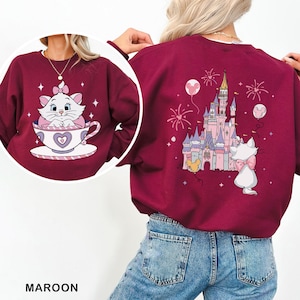 A person wearing a maroon sweater with a cat and castle design on it.