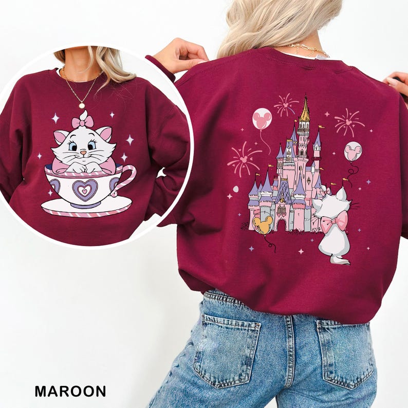 A person wearing a maroon sweater with a cat and castle design on it.