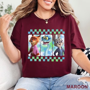 May include: Maroon t-shirt featuring three cartoon characters in a film strip design. The characters include a fox in a pink shirt, a blue snake, and a rabbit in a blue jacket. The shirt has a checkered border and the word "MAROON" at the bottom.