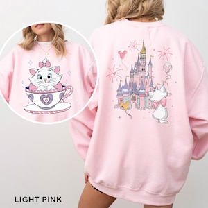 A woman wearing a pink sweatshirt with a cartoon image of a cat in a teacup and a castle on the back.