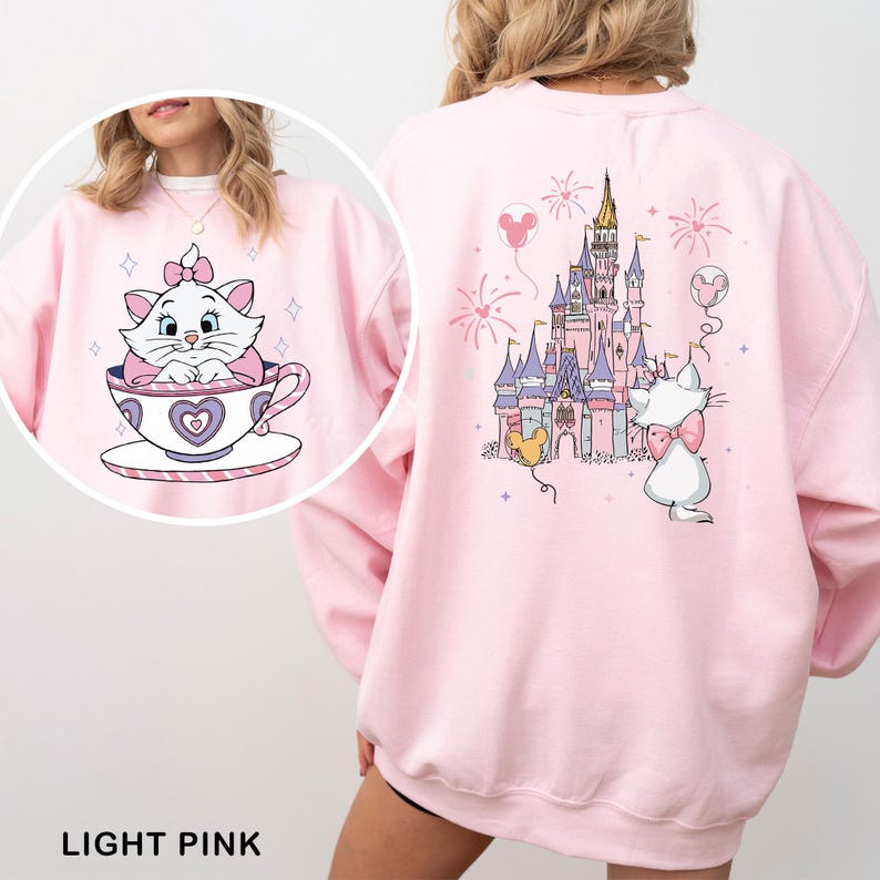 A woman wearing a pink sweatshirt with a cartoon image of a cat in a teacup and a castle on the back.