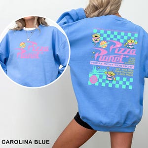 A woman wearing a blue sweatshirt with a graphic design featuring a cartoon character and text related to a pizza planet event.