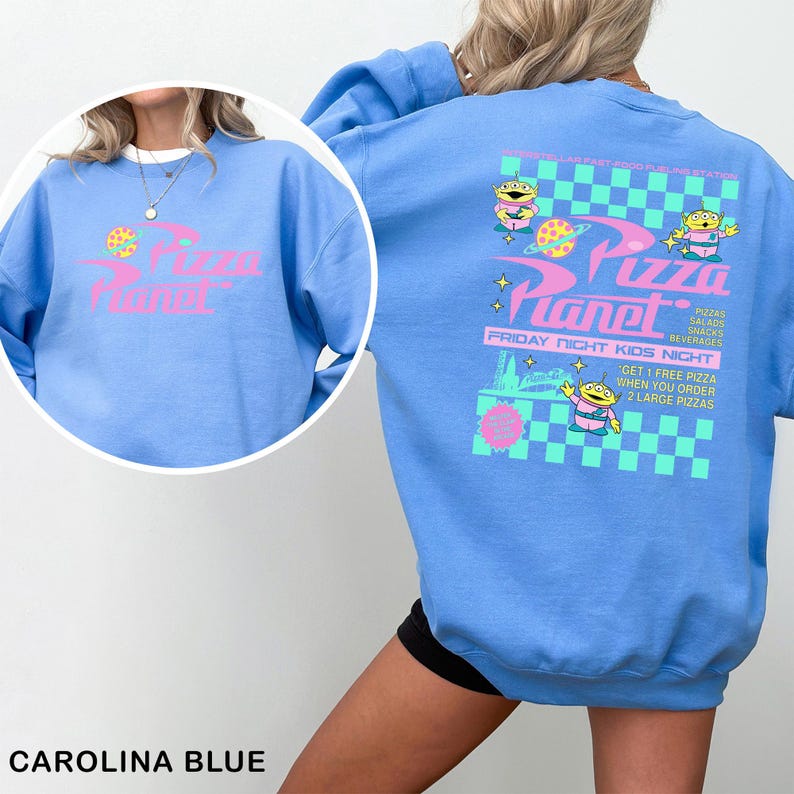 A woman wearing a blue sweatshirt with a graphic design featuring a cartoon character and text related to a pizza planet event.