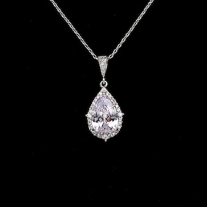 May include: A silver chain necklace with a pear-shaped pendant featuring a large clear crystal surrounded by smaller crystals.