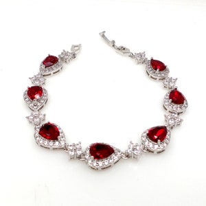 May include: A silver bracelet with a row of pear-shaped red gemstones surrounded by smaller clear gemstones.