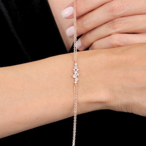 May include: A delicate rose gold bracelet featuring a cluster of sparkling clear gemstones. The bracelet is a fine chain design, with the gemstones clustered in the center. The bracelet is shown on a wrist against a black background.