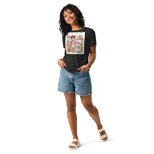 以下が含まれることがあります： 暗いヘザーグレーのTシャツに、キッチンにいる女性の漫画のイラストと「Eat in your T-Shirt」というテキストがプリントされています。