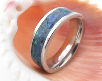 May include: A silver ring with a blue and green opal inlay. The ring is sitting on a pink seashell.