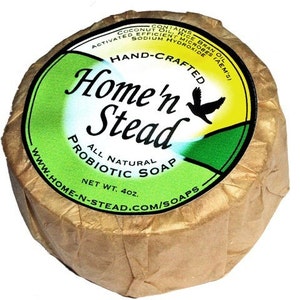 May include: A round bar of natural probiotic soap wrapped in brown paper. The label is green and yellow with the text "Home'n Stead" and a bird logo. The soap is 4 oz.