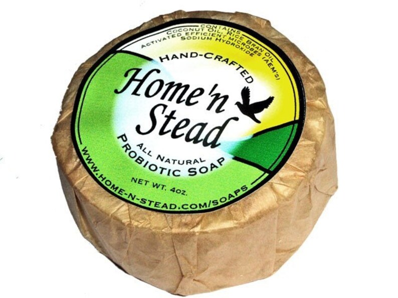 May include: A round bar of natural probiotic soap wrapped in brown paper. The label is green and yellow with the text "Home'n Stead" and a bird logo. The soap is 4 oz.
