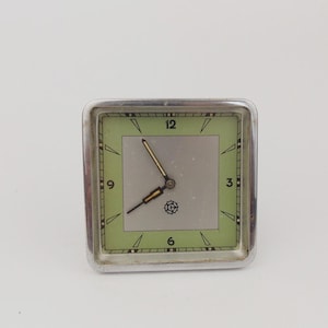 May include: A vintage square clock with a silver frame. The clock face has a light green border with black numerals and a silver centre. The clock hands are black and gold. The clock is set to approximately 2:40.