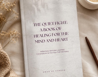 May include: A book titled "The Quiet Fight: A Book of Healing for the Mind and Heart" with dark purple text. The book is on a light-coloured surface, beside a cup of coffee and a pen. The book's cover has a textured, off-white appearance.