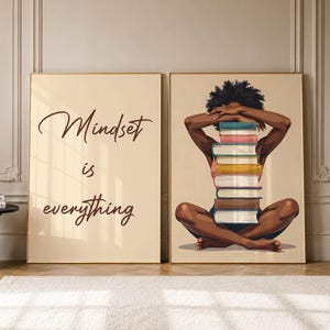 May include: Two framed wall art prints. The left print features the dark brown text "Mindset is everything" on a beige background. The right print depicts a person with dark skin and curly hair sitting cross-legged, holding a stack of books.