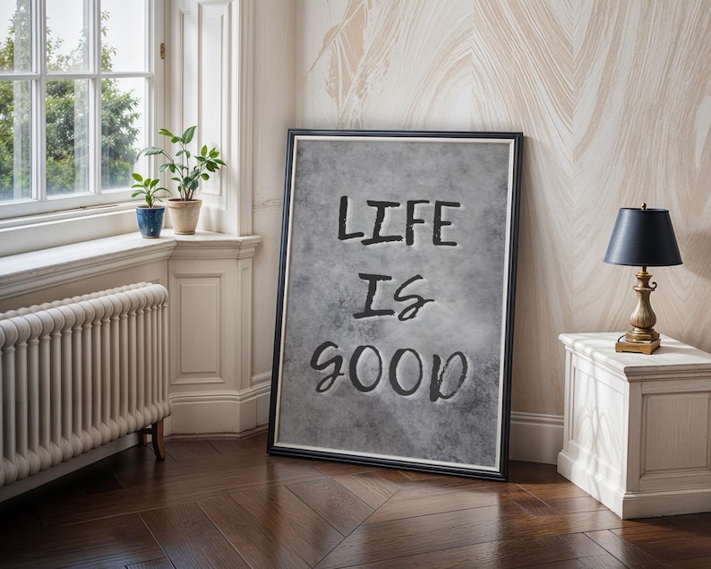May include: A rectangular framed wall art piece featuring a textured gray background with the black text "LIFE IS GOOD" centered in the middle. The artwork is enclosed in a thin black frame with a white inner border, displaying a clean design.