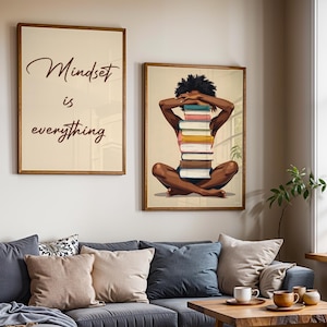 May include: Two framed art prints. One reads "Mindset is everything" in a cursive font. The other depicts a person with a stack of books. The art is displayed above a gray sofa with pillows and a wooden coffee table.