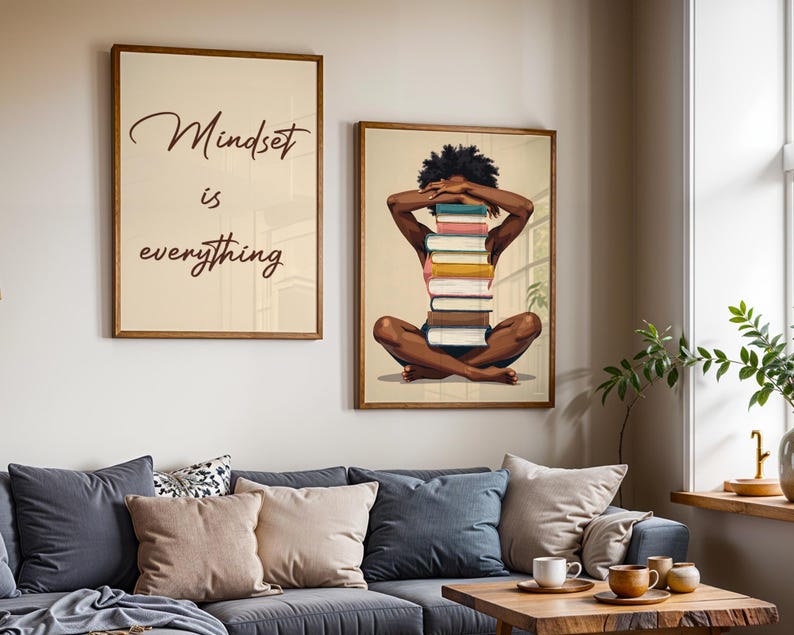 May include: Two framed art prints. One reads "Mindset is everything" in a cursive font. The other depicts a person with a stack of books. The art is displayed above a gray sofa with pillows and a wooden coffee table.