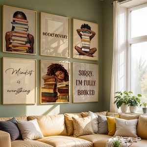 May include: A selection of framed art prints with images of people and books, alongside motivational quotes. The prints are displayed on a green wall above a tan sofa. The art has gold frames.
