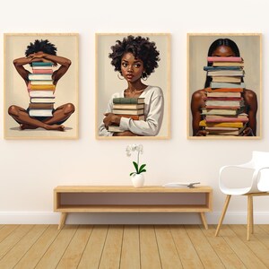 May include: Set of three framed art prints featuring illustrations of Black women with stacks of books. One figure sits cross-legged with books covering their face, another holds books, and the third has books in front of their face.