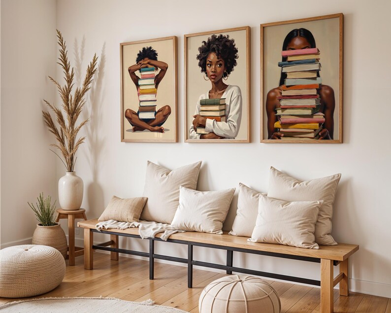 May include: Three framed art prints featuring illustrations of people with stacks of books. The artwork has a neutral color palette with wooden frames. The room also includes a wooden bench with pillows, a vase with tall grass, and a round ottoman.