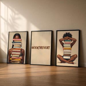 May include: Three framed art prints. The first shows a person with a stack of books in front of their face. The second print has the word "BOOKTROVERT". The third print shows a person with a stack of books in front of their face.