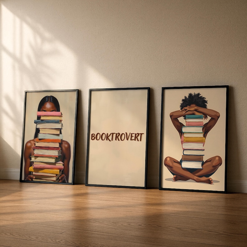 May include: Three framed art prints. The first shows a person with a stack of books in front of their face. The second print has the word "BOOKTROVERT". The third print shows a person with a stack of books in front of their face.