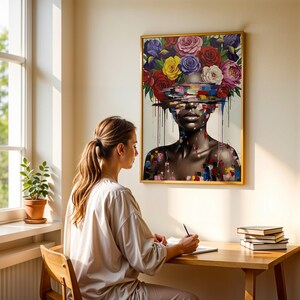 May include: A framed artwork shows a woman with a floral headdress of roses in various colours. The woman's face is partially obscured by colourful brushstrokes. The artwork is displayed on a wall above a wooden desk.