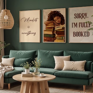 May include: A living room with three framed prints, one reading 'Mindset is everything', another showing a woman sleeping on books, and the third saying 'Sorry, I'm fully booked'. The room has a green sofa, beige cushions, and a wooden coffee table.